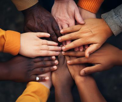 many human hands of different racial backgrounds are folded in a circle